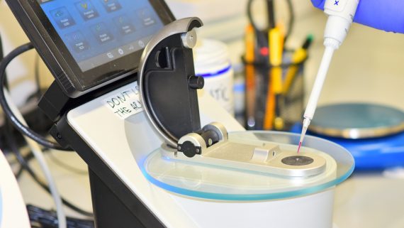 A scientist using a nanodrop device with a touchscreen to measure liquid samples in a laboratory setting.