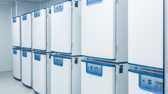 Laboratory equipment storage with multiple white temperature-controlled freezers lined against the wall.
