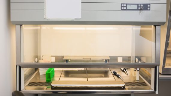 A laboratory workbench with a clear enclosure, equipped with pipettes and a green sample rack.